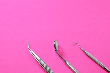 Diş hekimi araçları: ayna, diş sonda ve cımbız pembe degrade arka plan üzerinde.