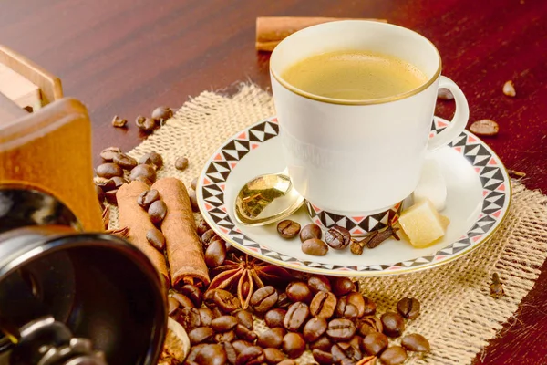 Coffee cup with saucer on a jute napkin. Vintage still life on wooden table with sugar, anise, cinnamon and dropped coffee beans — Stock Photo, Image