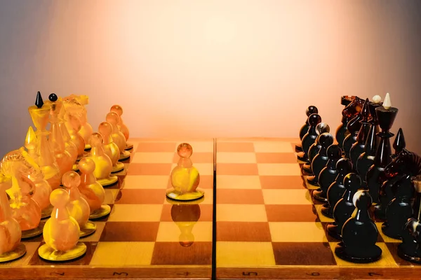 Schachspiel mit bernsteinfarbenen Schachfiguren auf dem Brett auf weißem Tisch, erster Zug e2-e4. mit goldenem Hintergrund. — Stockfoto
