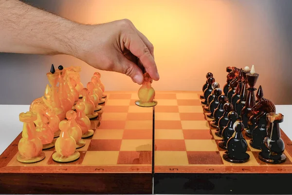Gra szachowa z bursztynowym kawałkami szachów na planszy. Pierwszy ruch, ręka gracza trzyma białą figurę. Ze złotym tłem gradientu. — Zdjęcie stockowe