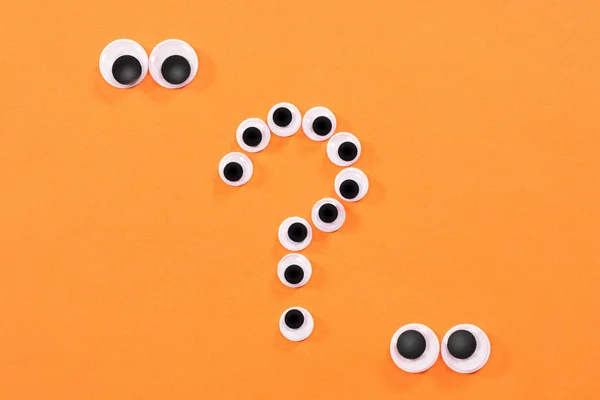 Googly eyes. Two strange persons with mad eyes look at some crazy toy eyes on orange background in the shape of question mark.