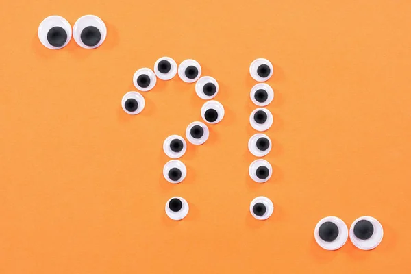 Googly eyes. Two strange persons with mad eyes look at some crazy toy eyes on orange background in the shape of question and exclamation marks.