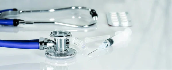 Stetoskop lub fonendoskop na białym biurku lekarza ze strzykawką i lekami. Leczenie zimna lub grypy, rozmiar wstęgi — Zdjęcie stockowe