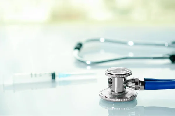 Stetoskop lub fonendoskop na białym biurku lekarza w pobliżu okna ze strzykawką. Leczenie przeziębienia lub grypy. — Zdjęcie stockowe
