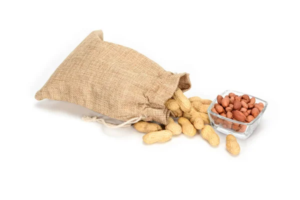 Grondnoten. Jute jute zak vol met pinda's en glazen kom met geschilde kernels, geïsoleerd op witte achtergrond. — Stockfoto