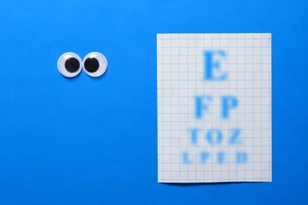 Cross-eyed googly eyes on blue background with sight check table. Mad funny toys eyes close up.