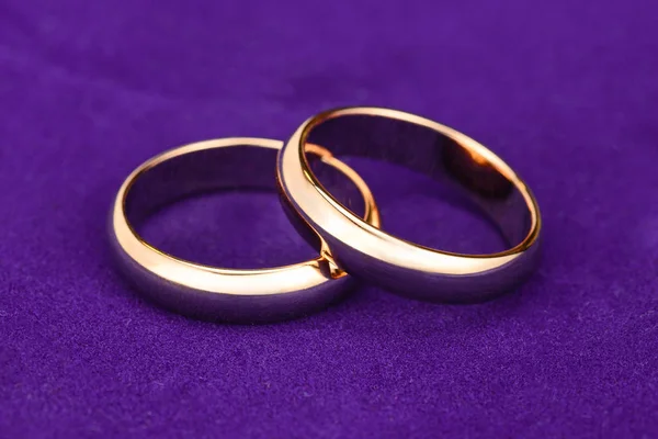 Two gold wedding rings. Engagement rings close up on violet velvet background, macro jewelry for newlyweds. — Stock Photo, Image