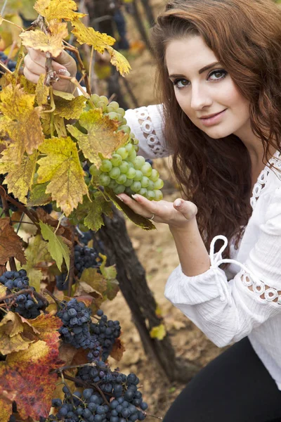 Young woman squatting, holding green grapes and looking at camera. There are two sorts, green and dark blue.