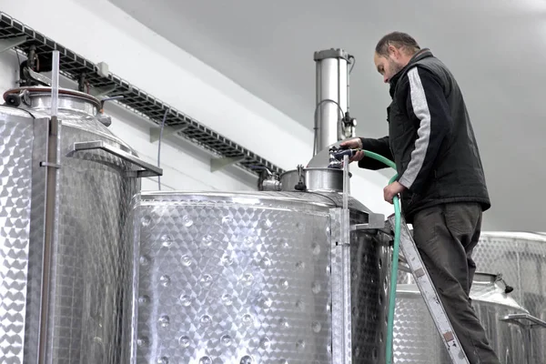 Worker in wine production is cleaning a big fermentation wine tank. Stainless steel tanks for a fermentation on are in modern manufacture of wine making.