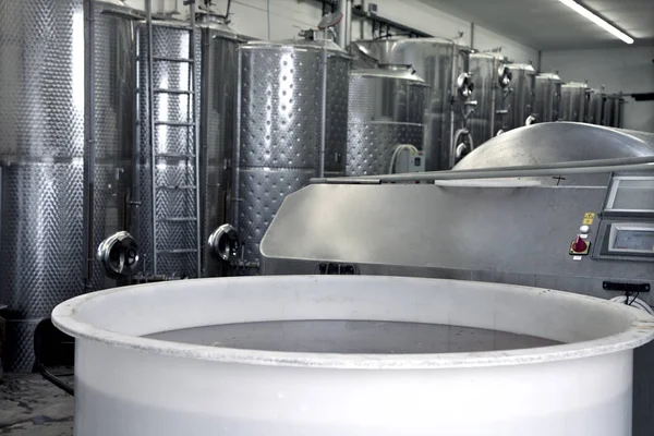 Big plastic container full of wine. Stainless steel tanks for a fermentation on background. Modern manufacture of wine making.