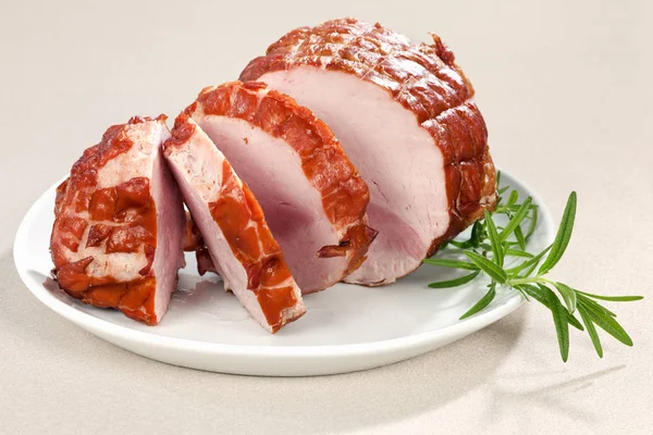 Roll of smoked ham on plate. Decorated with rosemary. The bread is on backgroud. Selective focus.