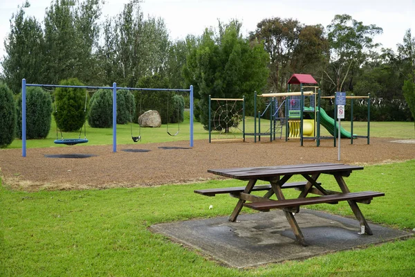 Playground with wooden park bench in the forground — Stock Photo, Image