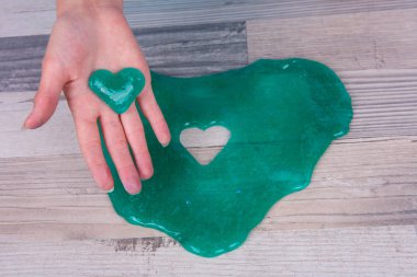 Ahşap arka plan önünde kalp şekli yeşil sümük çamur ile yardım