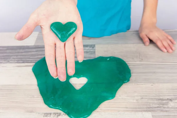 Girl created a heart shape slime with a cookie cutter and showing it on her palm