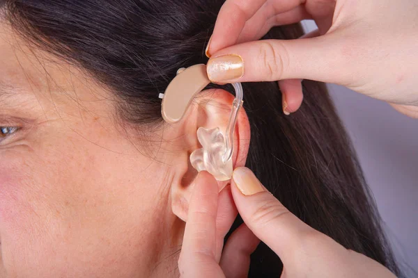 Close up of hands inserting hearing aid in a woman\'s ear