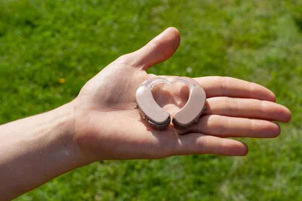Close up of hearing aids arranged in heart shape on hand in fron — Stockfoto