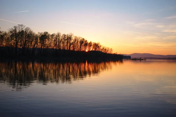 Puesta de sol en colores fuertes sobre un río con reflejos de árboles — Foto de Stock