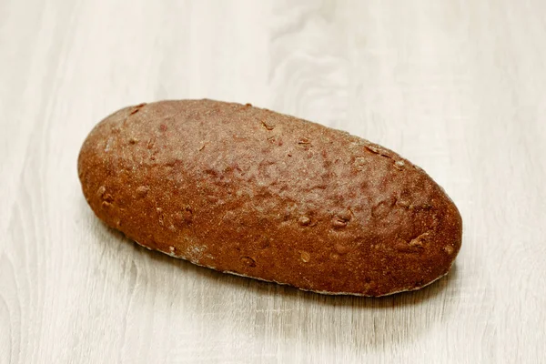 Een zwart gebakken brood op een lichte houten achtergrond — Stockfoto