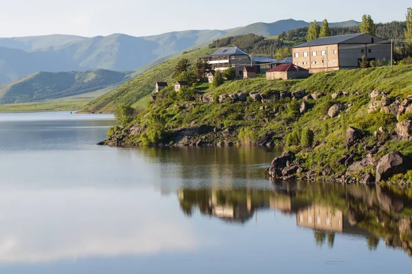 Lago contra el fondo de las montañas durante el día con edificios residenciales de la costa verde — Foto de Stock