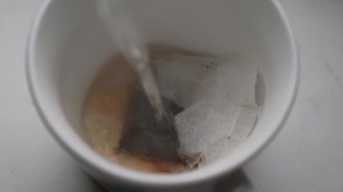 kaynar su tek kullanımlık çay poşeti üst görünümü ile bir bardağa dökülür