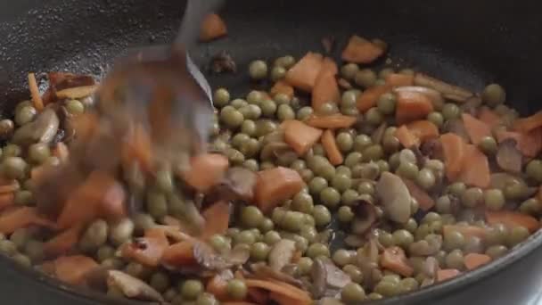 Wortelen met champignons en groene erwten om in een pan te bakken — Stockvideo