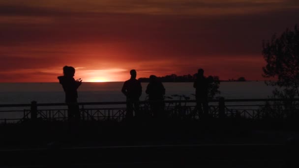 Силуети людей на міській набережній під час заходу сонця — стокове відео