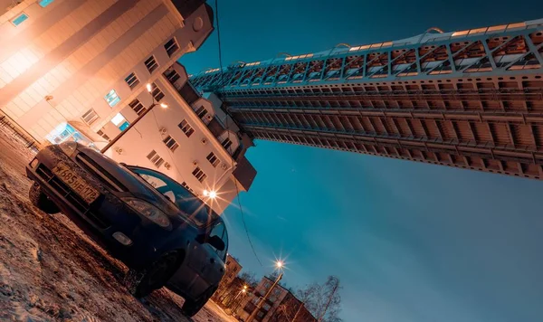 Blue car on the background of a multi storey building and under the bridge in the evening in winter — Stock Photo, Image