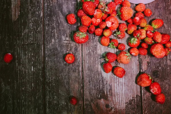 Fresas esparcidas en una vieja mesa de madera — Foto de Stock