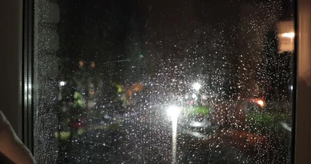 Okna wielopiętrowego budynku w deszczu spada z widokiem na ulicę nocy — Wideo stockowe