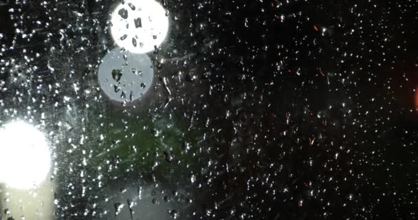 Esőcseppek az üvegen szemben a fény az éjszakai fények bokeh — Stock videók