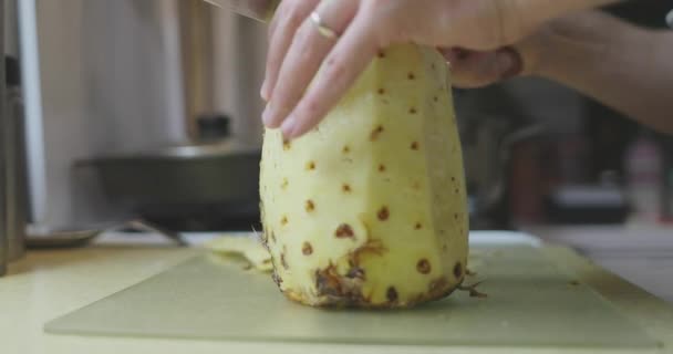 手はナイフを持ち、台所のテーブルの上にパイナップルを切る — ストック動画
