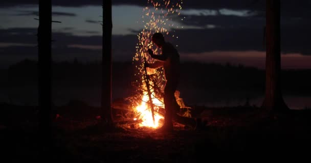 男は投げ出し、夜に明るい炎ですでに燃えている火を改善します — ストック動画