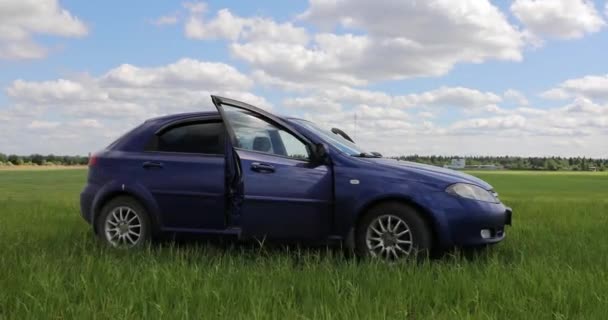 Niebieski samochód w zielonym polu przed niebem — Wideo stockowe