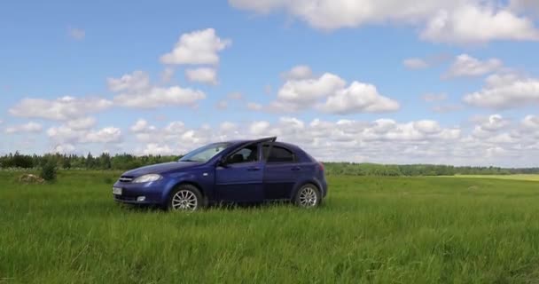 Blå bil i ett grönt fält mot himlen — Stockvideo