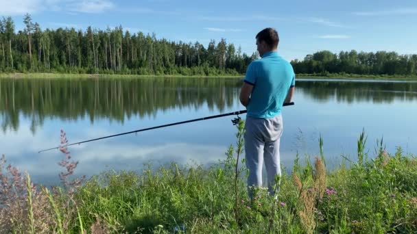 Ένας άντρας στέκεται δίπλα στη λίμνη και ψαρεύει μια ηλιόλουστη μέρα. — Αρχείο Βίντεο