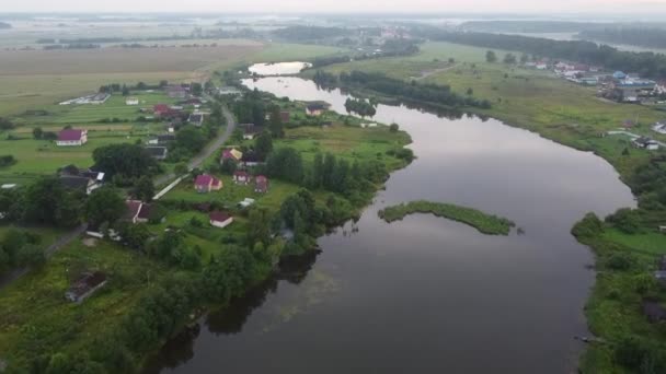 Kis falu a folyó közelében egy nyári esti légi felvételen — Stock videók