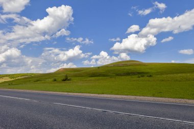 Alan, şehirlerarası izi alanında yolda. Güzel yeşil tepeler. Kabarık bulutlar ile mavi gökyüzü.