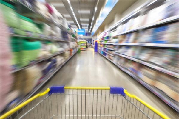Blurred photos showcases shops on the background of a grocery cart. Long rows of racks with goods.