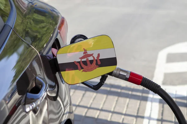Flag of Brunei on the car\'s fuel tank filler flap. Fueling car with petrol pump at a gas station. Petrol station. Gasoline and oil products. Close up.