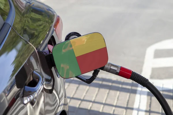 Flag of Benin on the car\'s fuel tank filler flap. Fueling car with petrol pump at a gas station. Petrol station. Gasoline and oil products. Close up.