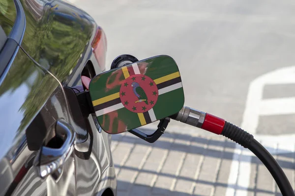 Flag of Dominica on the car\'s fuel tank filler flap. Fueling car with petrol pump at a gas station. Petrol station. Gasoline and oil products. Close up.
