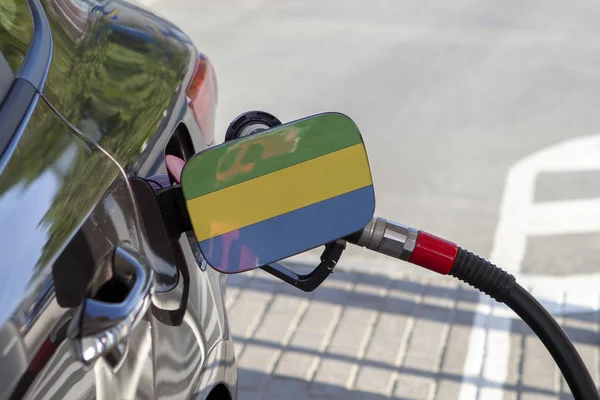 Flag of Gabon on the car\'s fuel tank filler flap. Fueling car with petrol pump at a gas station. Petrol station. Gasoline and oil products. Close up.