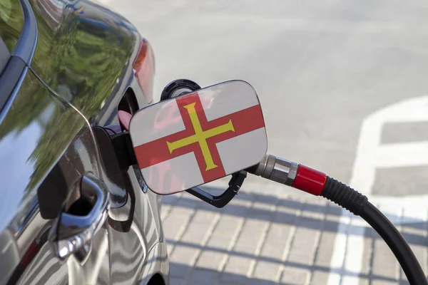 Flag of Guernsey on the car\'s fuel tank filler flap. Fueling car with petrol pump at a gas station. Petrol station. Gasoline and oil products. Close up.