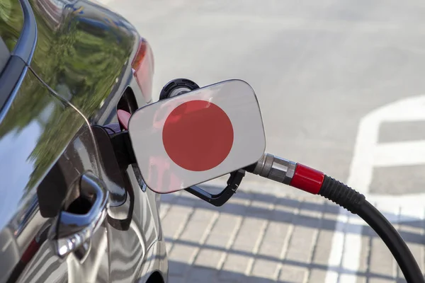 Flag of Japon on the car\'s fuel tank filler flap. Fueling car with petrol pump at a gas station. Petrol station. Gasoline and oil products. Close up.