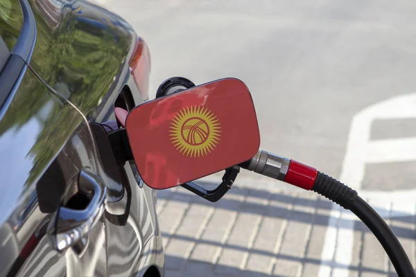 Flag of Kyrghyzstan on the car's fuel tank filler flap. Fueling car with petrol pump at a gas station. Petrol station. Gasoline and oil products. Close up.
