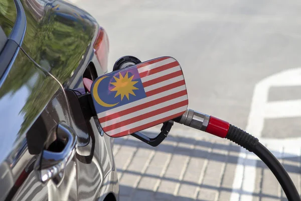Flag of Malaisie on the car\'s fuel tank filler flap. Fueling car with petrol pump at a gas station. Petrol station. Gasoline and oil products. Close up.