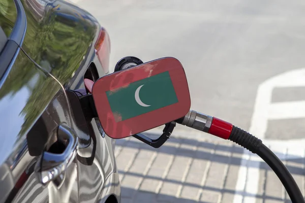 Flag of Maldives on the car\'s fuel tank filler flap. Fueling car with petrol pump at a gas station. Petrol station. Gasoline and oil products. Close up.