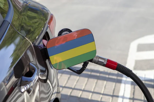 Flag of Mauritius on the car\'s fuel tank filler flap. Fueling car with petrol pump at a gas station. Petrol station. Gasoline and oil products. Close up.