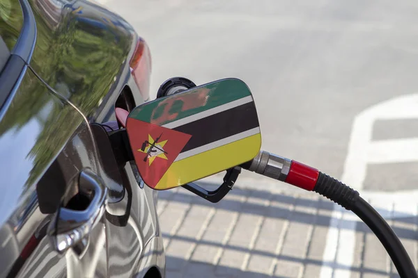 Flag of Mozambique on the car\'s fuel tank filler flap. Fueling car with petrol pump at a gas station. Petrol station. Gasoline and oil products. Close up.