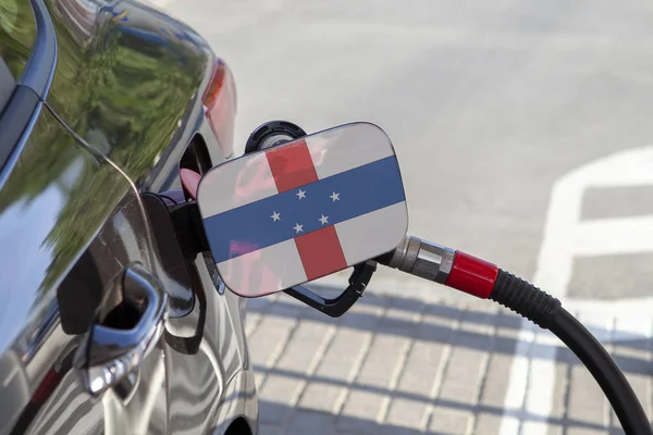 Flag of  Netherlands Antilles on the car's fuel tank filler flap. Fueling car with petrol pump at a gas station. Petrol station. Gasoline and oil products. Close up.